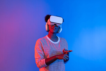 Smiling enthusiastic young African woman wearing VR headset surprising through metaverse world at...