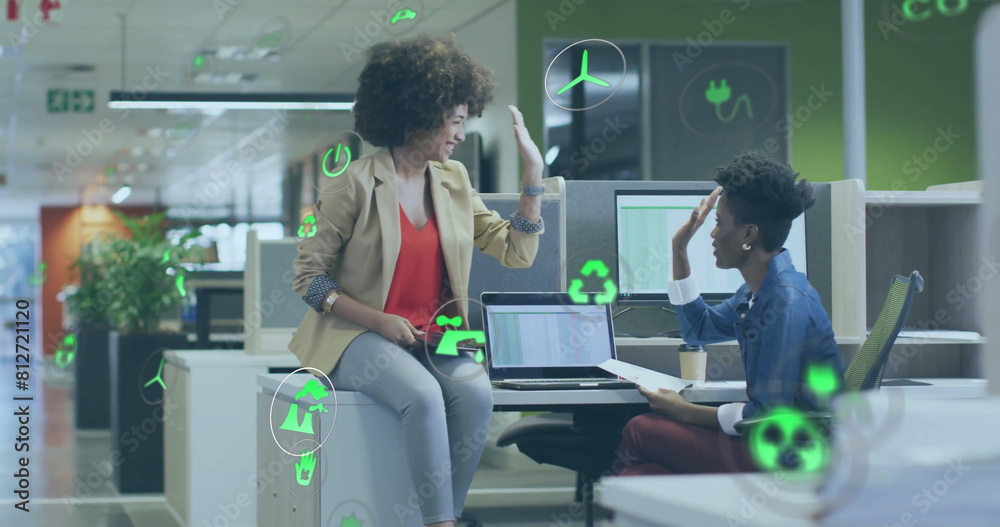 Wall mural Image of icon in circles over diverse female coworkers discussing and giving high five on desk