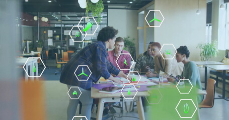 Image of icon in hexagons over diverse coworkers sharing ideas in office