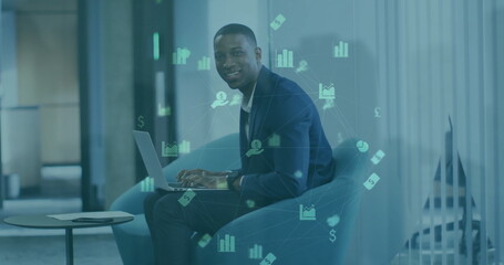 Image of graphs and financial icons over african american businessman using laptop on armchair