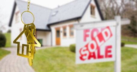 Image of gold house key fob and key, hanging in front of blurred house with sold sign