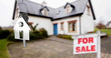 Image of silver house key fob and key, hanging in front of blurred house with for sale sign