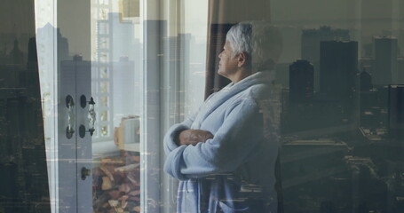 Image of senior biracial woman looking through window over cityscape - Powered by Adobe