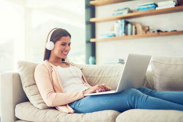 Woman, laptop and happy with headphones on sofa in home for audio streaming, subscription service...