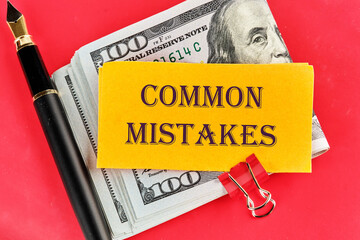 Common mistakes, text on a sticker lying on dollar bills on a red background, next to a fountain pen
