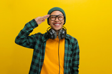 A young Asian man, dressed in a beanie hat and casual clothes, salutes with a cheerful expression...
