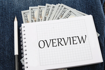 OVERVIEW written on a notebook lying on jeans with dollar bills