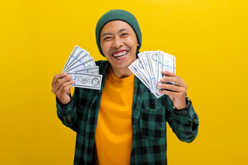 Excited Asian man in a beanie and casual clothes holds banknotes in his hand. Isolated on a bright...