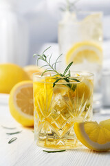 Summer refreshing lemonade drink or alcoholic cocktail with ice, rosemary and lemon slices on the white table.