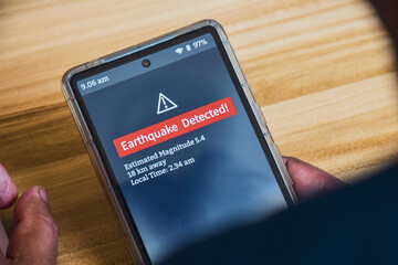 Fototapeta na wymiar Man hand holding his mobile phone displaying Earthquake detection alert notification. Close up view.