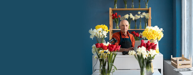 old man florist small business owner of flower shop sitting at workplace in boutique working using...
