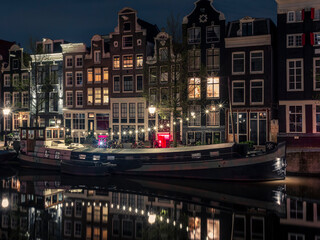 An illuminated houseboat reflecting in the Singel canal in Amsterdam at night