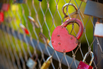 red love padlock heart is hanging from a chain link fence