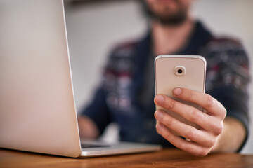 Smartphone, laptop and hand at desk for work, online and multitask in home office. Cellphone, app and man on computer for checking information, email or research notes or networking on internet
