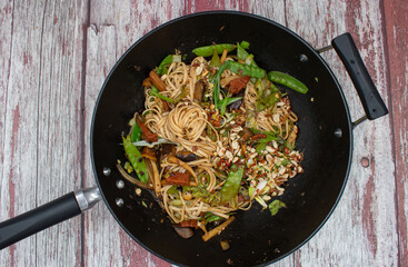A delicious vegan stir fry consisting of seitan, eggplant, snow peas and other greens stir fried in steel wok, served along with noodles