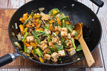 Vegan stir fry cooked in cast iron wok. Tofu, pepper, asparagus, greens served along with stir...