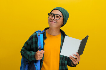 A happy young Asian student, dressed in a beanie hat and casual clothes, sporting eyeglasses and...