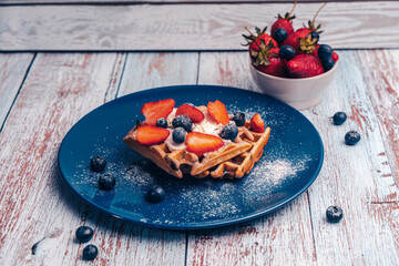 A delicious dessert for breakfast. Belgian waffles with strawberries and blueberries, sprinkled...