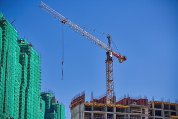 Tower crane on construction site against blue sky. Tall building under construction. Real estate construction. Concept of urban development and architecture.