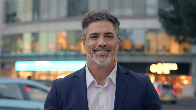 Mature hispanic senior business man standing on busy city street. Headshot close up portrait of Indian or latin confident good looking middle age male entrepreneur businessman happy smiling at camera.
