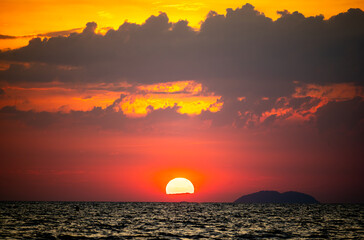 fiery sunset over ocean, with vibrant shades of orange and red painting sky. sun sets dramatically,...