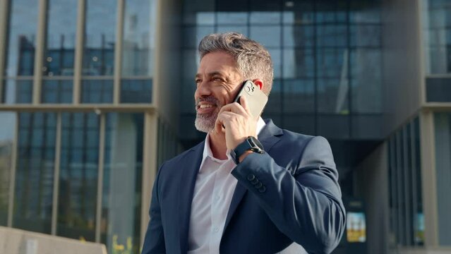40s mature confident busy businessman entrepreneur using cellphone mobile phone for talking with client, business partners. Successful mid age man investor communicating on smartphone standing outdoor
