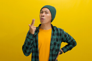 Young Asian man, dressed in a beanie hat and casual shirt, makes a finger gun gesture, mimicking...