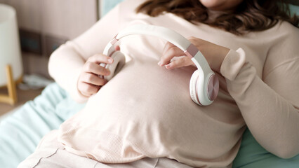 Pregnant asian woman using headphone on her belly playing music to her baby