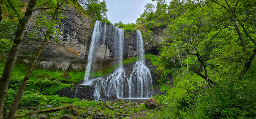 A beautiful waterfall cascade in France, surrounded by trees, rocks and grass