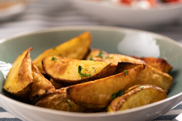 Roasted potatoes. Baked potato wedges in plate on table, close-up.