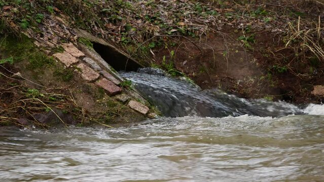 Water inflow into a dirty river during a rain period. High water levels in a rural area. An industrial facility is pumping the sewage into the environment.