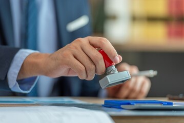 Fototapeta premium A person in a suit stamping a document with a red stamper.