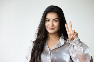 Happy, smiling, friendly south asian woman in pointing up 2 fingers, V for victory hand sign,...