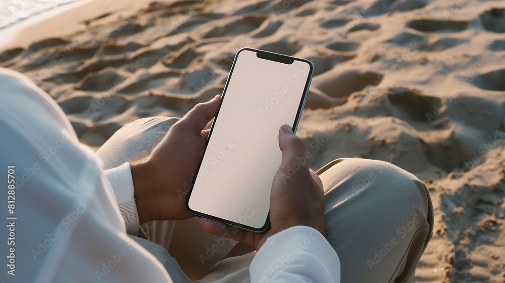 Fototapete mockup image of a man holding mobile phone with blank desktop screen while sitting on the beach : ge