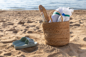 Jute bag with sunscreen bottle, beach towel with flip flops on the sand. Summer vacation lifestyle concept