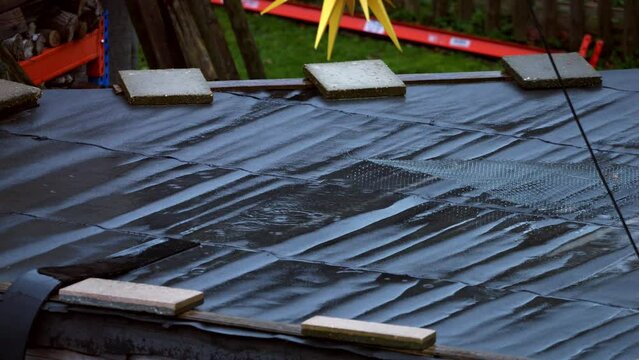 Rain drops on a rooftop with old roofing felt. Leaking and messy repaired roof with tar paper and trash lying around in a poor neighborhood.