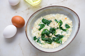 Bowl of stracciatella or egg-drop soup with spinach, horizontal shot on a light-beige marble background, high angle view