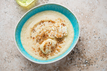 Turquoise bowl with roasted cauliflower cream-soup, horizontal shot on a beige granite background, high angle view