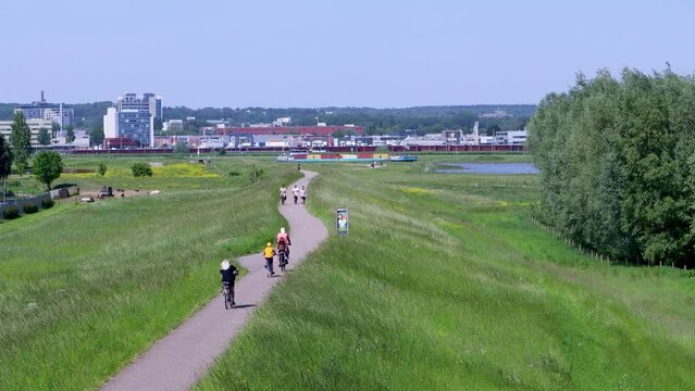 Cyclists and walkers on a dike in the Netherlands on a sunny day. A boat passes by on the Rhine river.