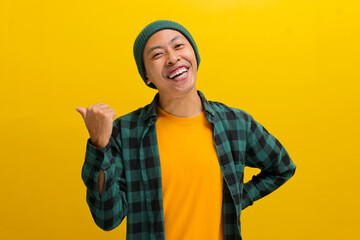 Happy, smiling young Asian man, dressed in a beanie hat and casual shirt, invites with a beckoning...