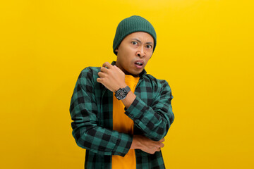 Displeased young Asian man, dressed in a beanie hat and casual shirt, is clearly expressing his disgust at something awful while standing against yellow background.