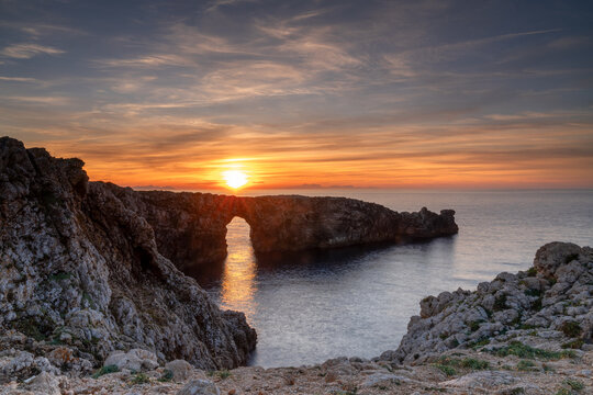 view of the landmark stone arch of Pont d'en Gil on Menorca Island at sunset