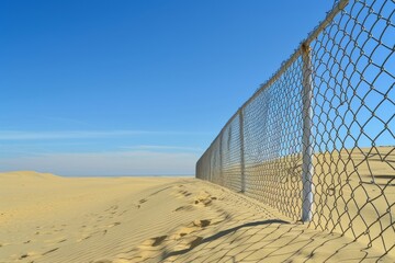 Obraz premium A fence is on a sandy beach with a clear blue sky