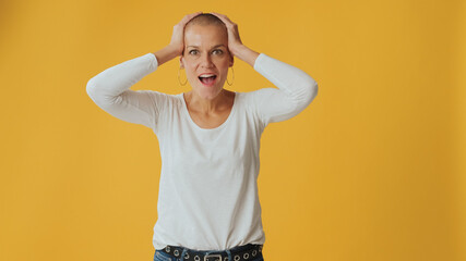 Shocked young hairless woman, looking at camera with big eyes, says wow, isolated on yellow...