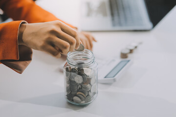 Beautiful Asian businesswoman insert coins in a pin piggy bank on the table. saving money,...