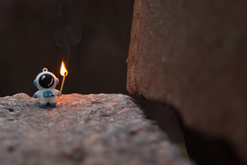 A toy astronaut with a match in his hand burns in nature
