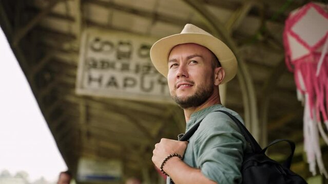 Asian travel blogger at Haputale railway station clicks with camera. Explorer captures local scenes, architecture, immersed in journey. Backpacker in hat surveys, photo ops around busy depot. Slowmo