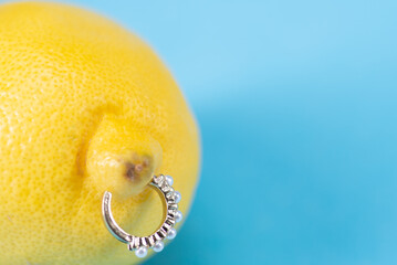 Intimate piercing. Minimal piercing concept. Lemon with piercing on blue background