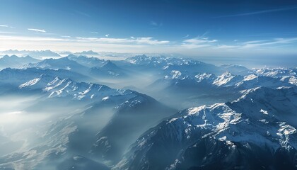 Aerial view of snowcapped mountains in the Alps, with misty peaks and a blue sky