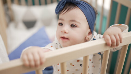 Adorable toddler standing on cradle with relaxed expression at bedroom